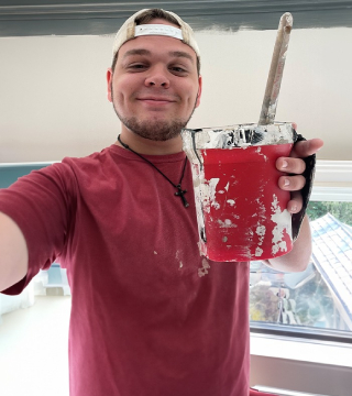 brandon Image of a man holding a small bucket of paint with a brush