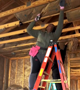 Female carpenter on a ladder working on framing a room