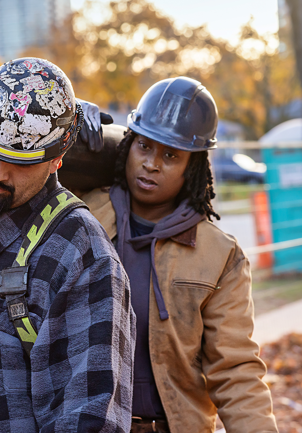Man and woman with hard hats carrying large pipe together over their shoulder