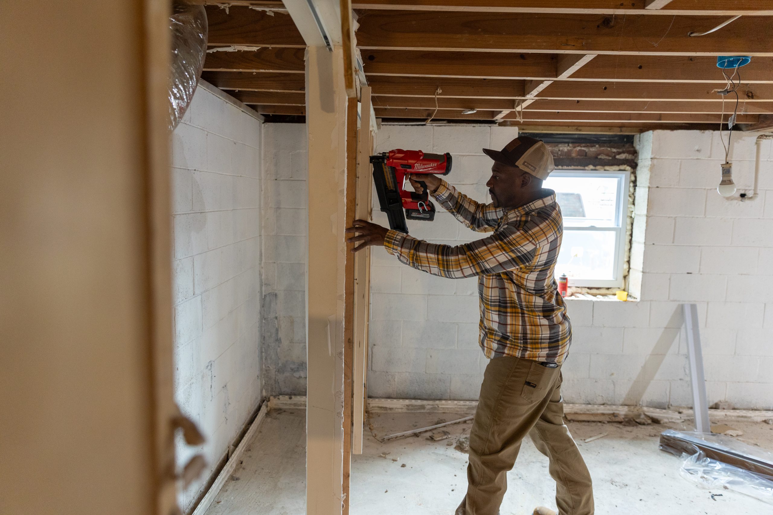 African American male using nail gun to nail interior framing in a basement