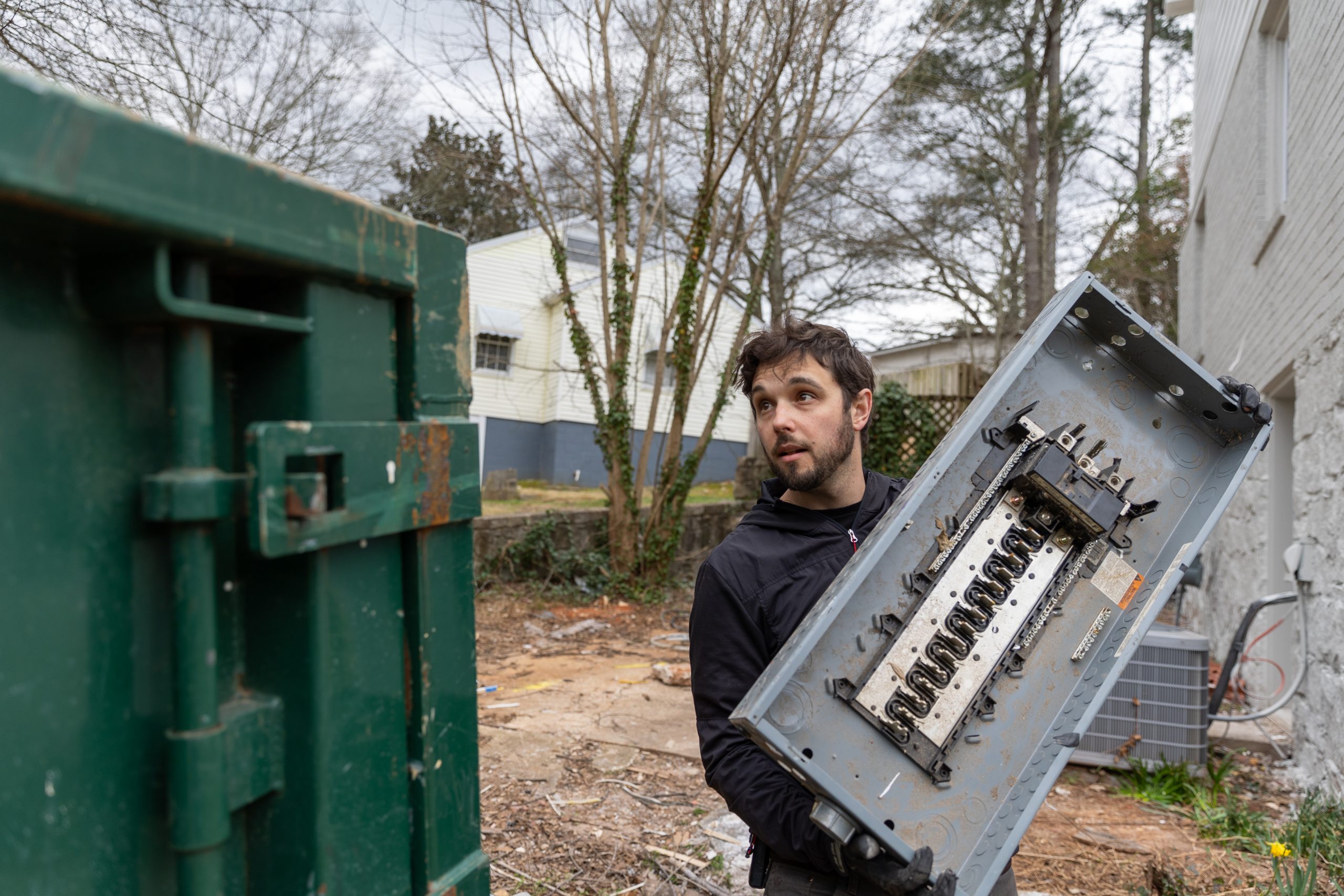 Caucasian male throwing an old electrical panel into a dumpster