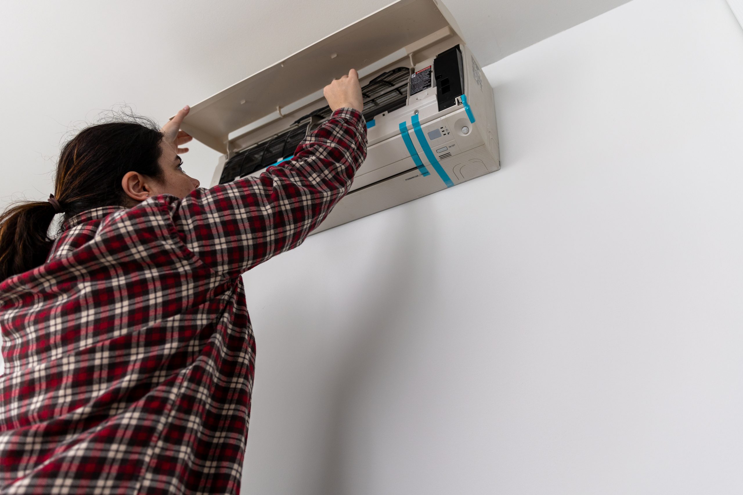 Mujer caucásica instalando una unidad de sistemas de calefacción, ventilación y aire acondicionado (HVAC) de tipo split