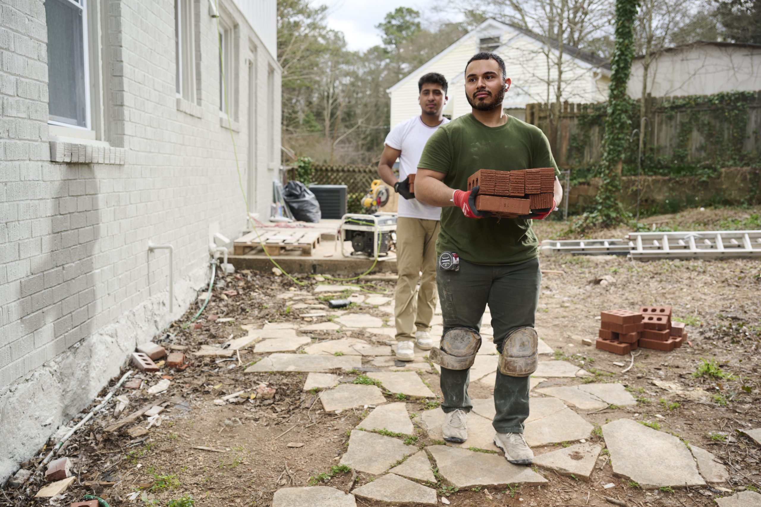 Two Hispanic males walking through a job site carrying bricks