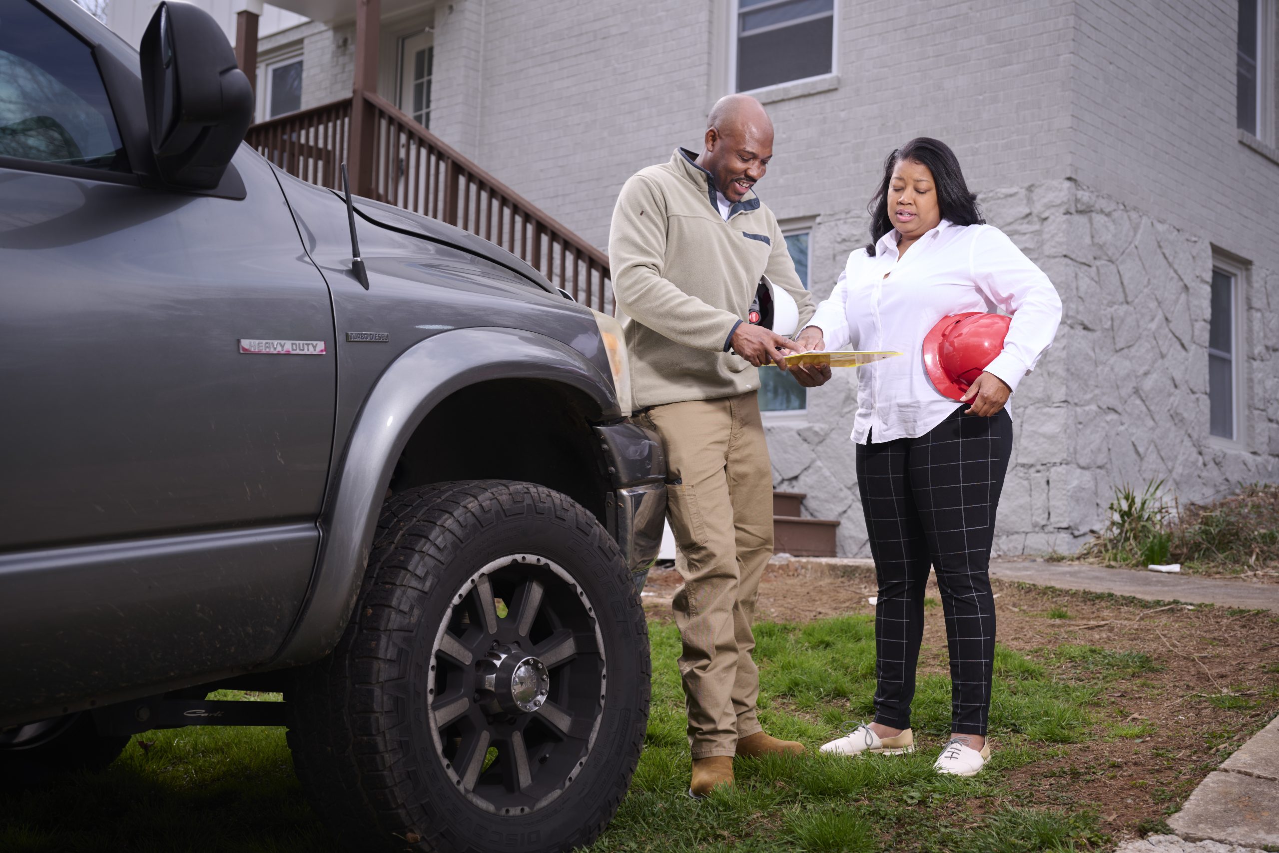 African American male and female reviewing construction plans by work truck in front of a house