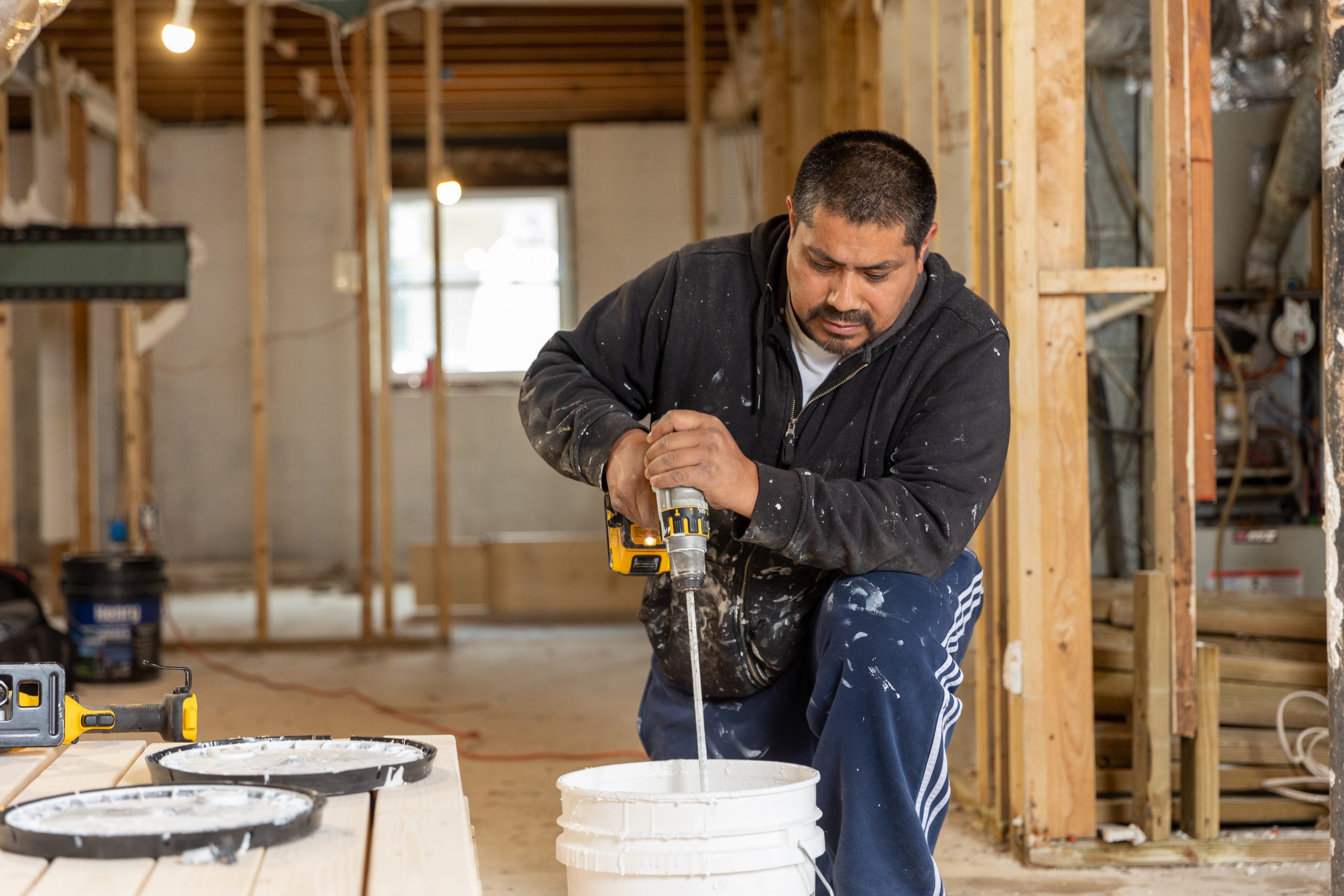 Hispanic male kneeling down using an electric mixer to mix paint