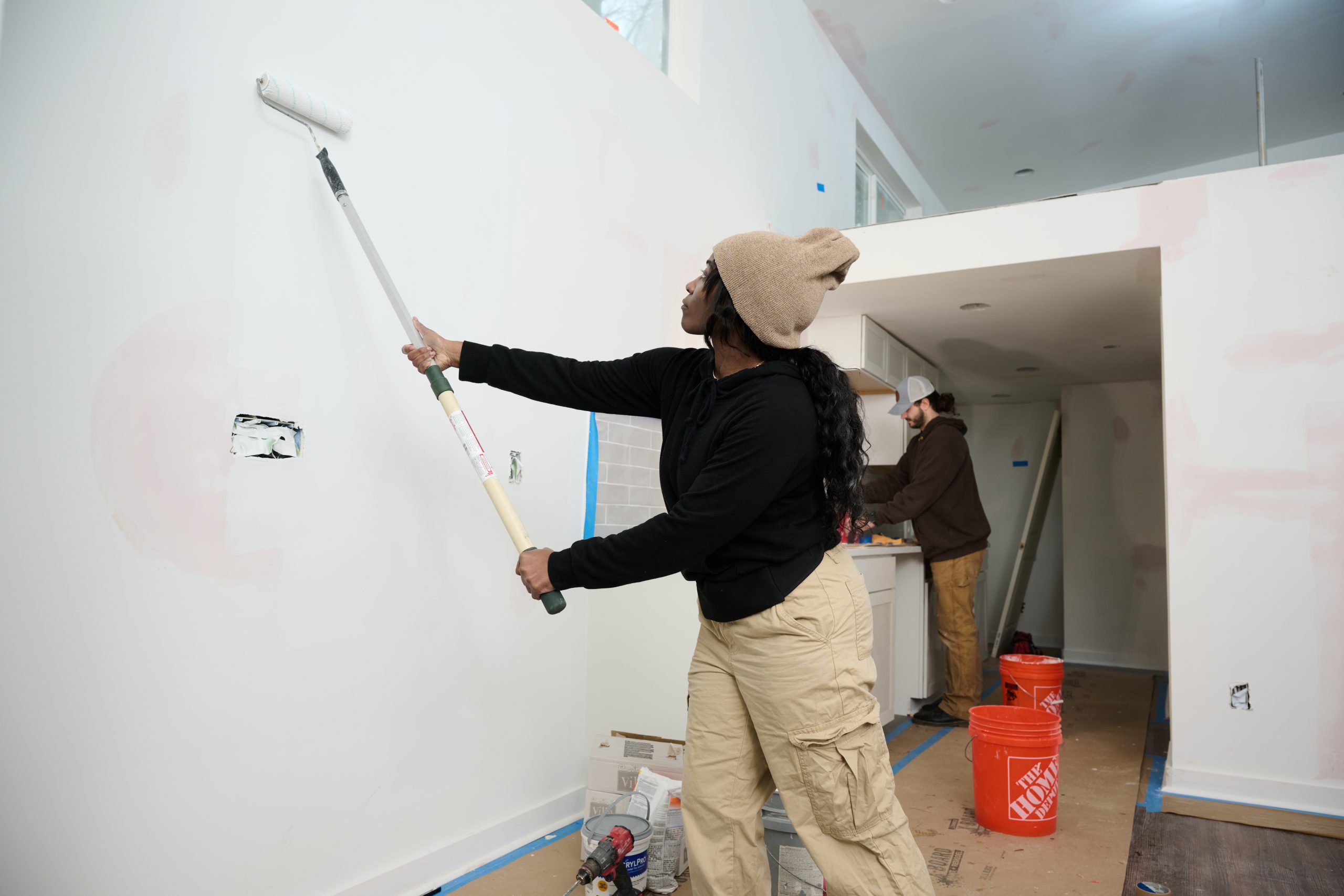 African American female using a long paint roller to paint a wall