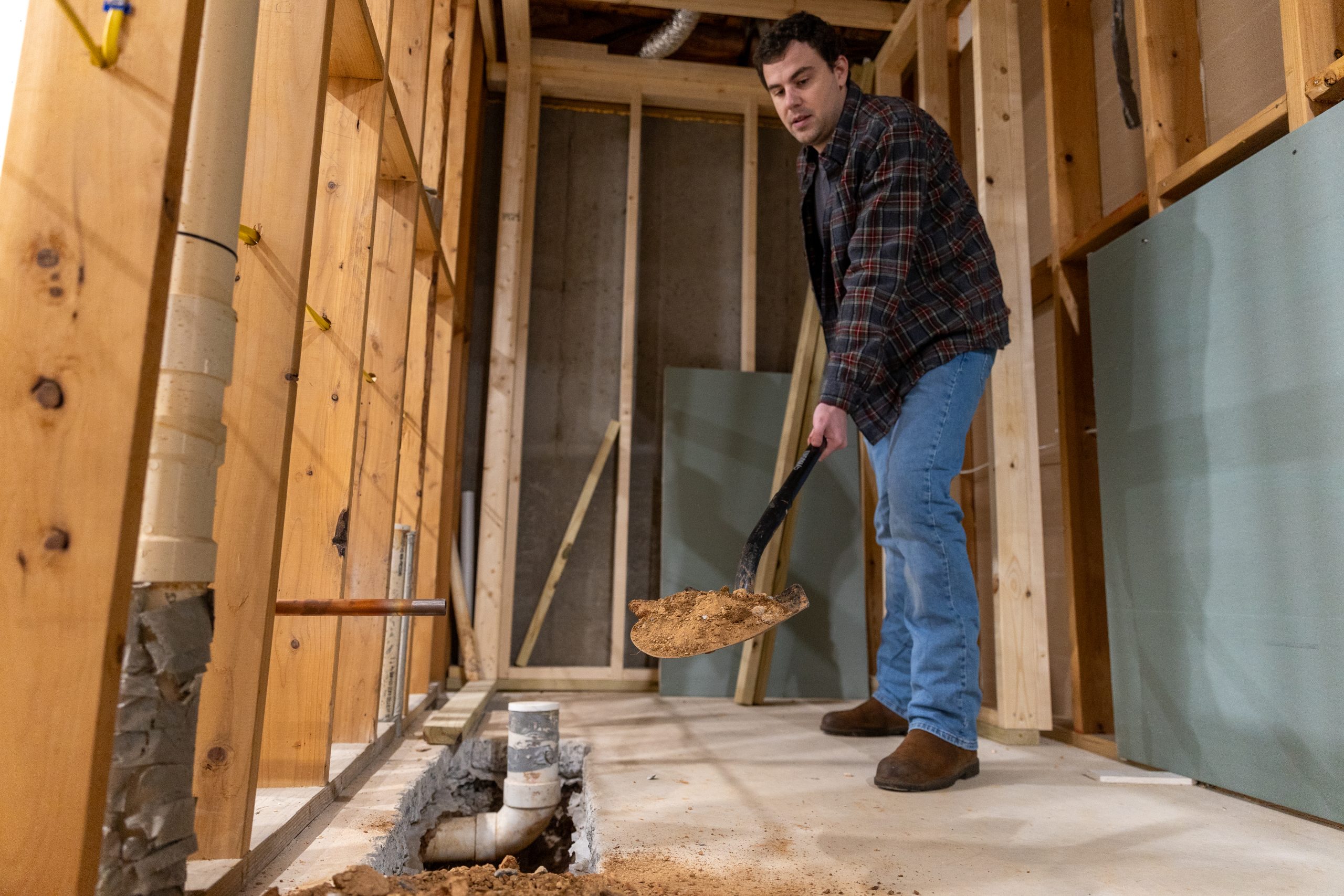 Caucasian male shoveling debris in an unfinished basement
