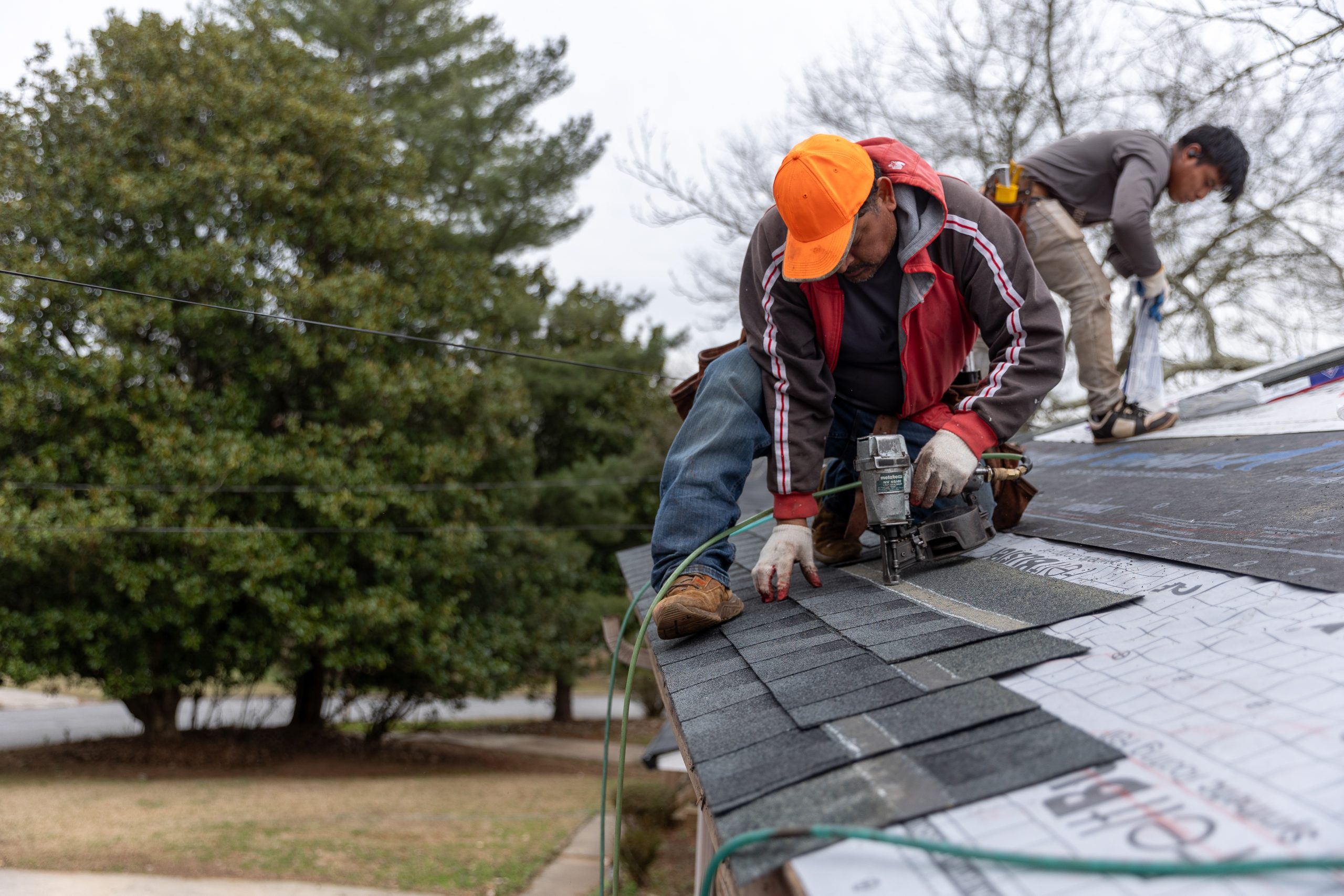 Two Hispanic males working to nail new shingles on a roof