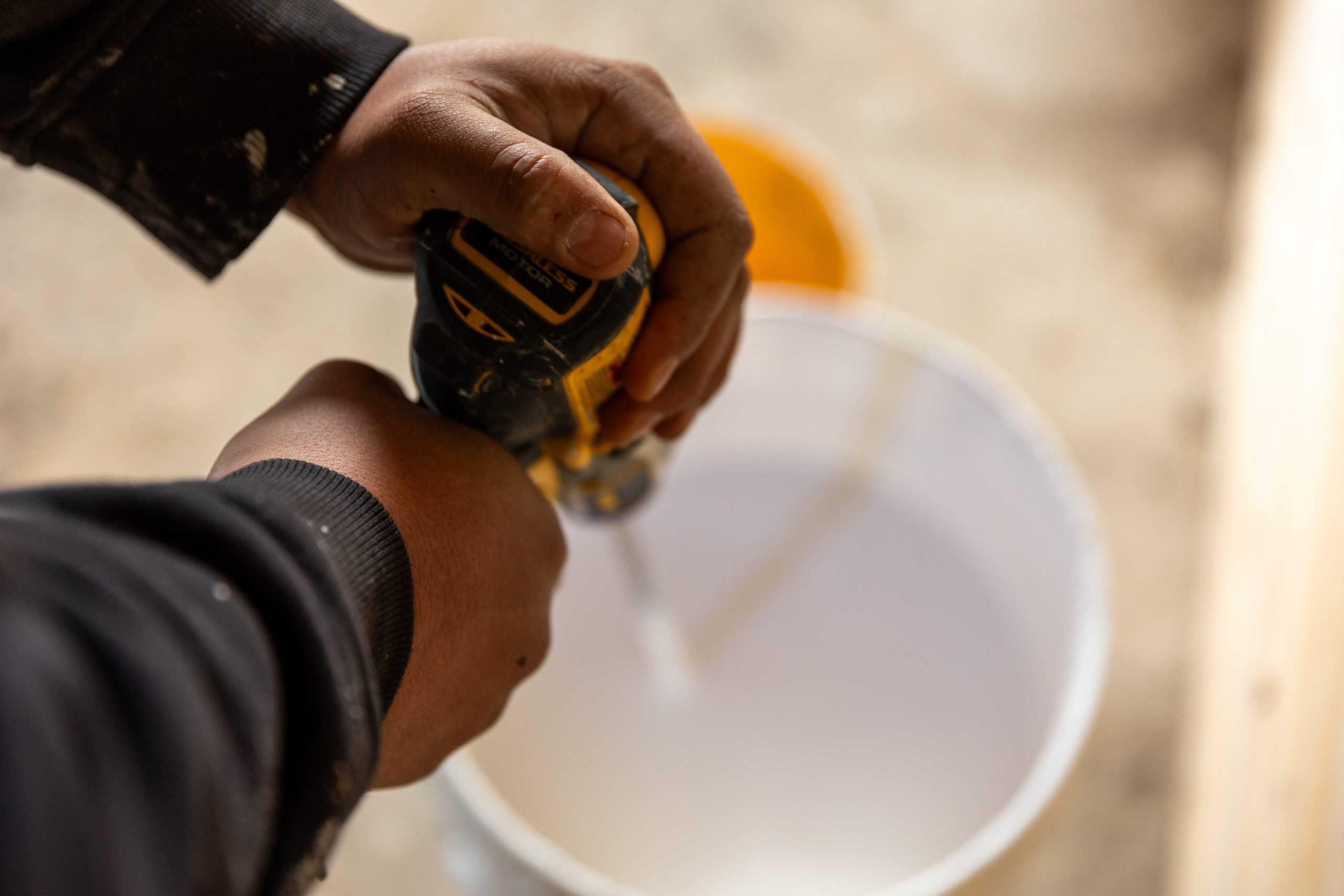 hands using an electric mixer to mix white paint in a bucket