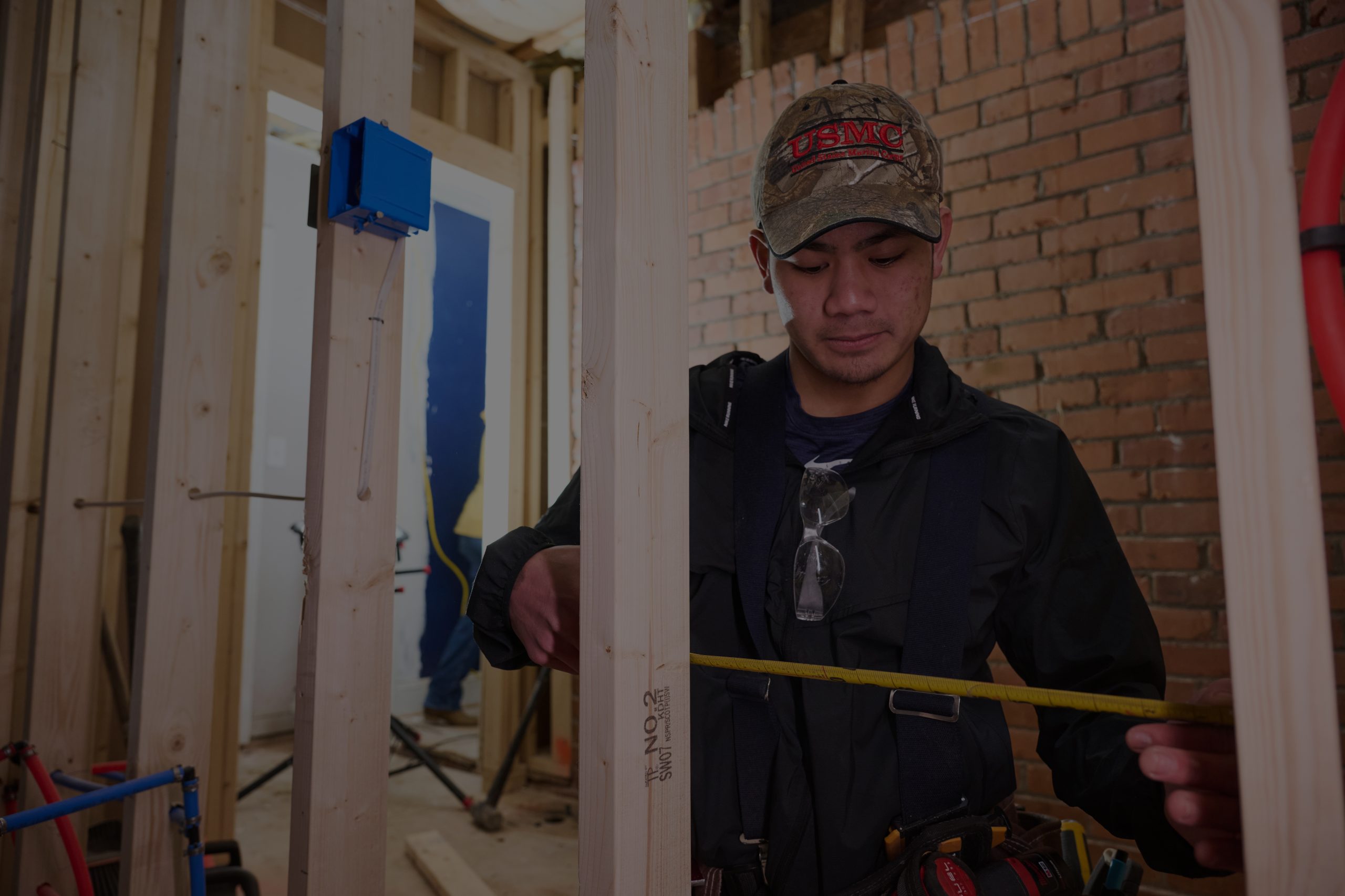 Asian male in a USMC hat using a measuring tape to measure interior framing